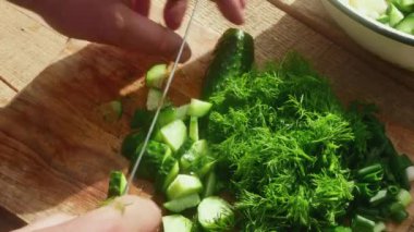 Bıçaklı el, salata için ahşap masadaki dereotunun yanında salatalık keser..