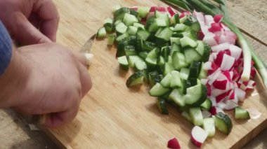  Bir adamın eli, salatalık ve turpun yanında tahta kesme tahtasına saplanmış bir bıçakla pırasa keser..