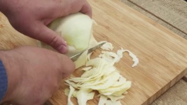 Bir adamın eli, tahta bir tahtanın üzerinde bıçakla lahana keser..