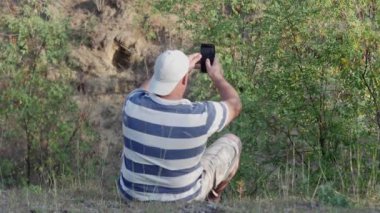  a man takes a selfie in the forest on the edge of a ravine, rear view.