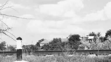 time lapse of the movement of white clouds over the old railway rails against the backdrop of a village in Eastern Europe, in black and white.