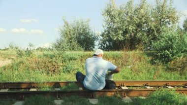 the traveler puts his laptop in his backpack and talks on the phone while sitting on the railroad tracks.