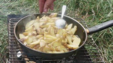 hand salting potatoes, fried in a frying pan on a grill, in a meadow.