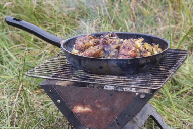 Kızartma tavasının yanındaki ızgarada tavuk budu ve yanında patates kızartması.