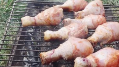 Terbiye edilmiş tavuk budu dumanla kaplanmış açık bir alanda ızgarada, yakın plan.