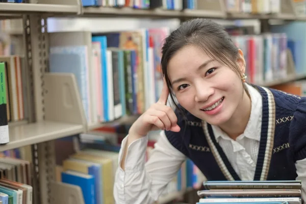 Ung student håller böcker nära bokhylla — Stockfoto