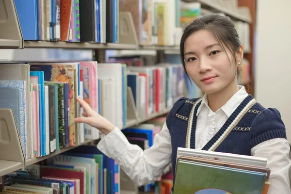 Vrouw op zoek naar boeken van plank — Stockfoto