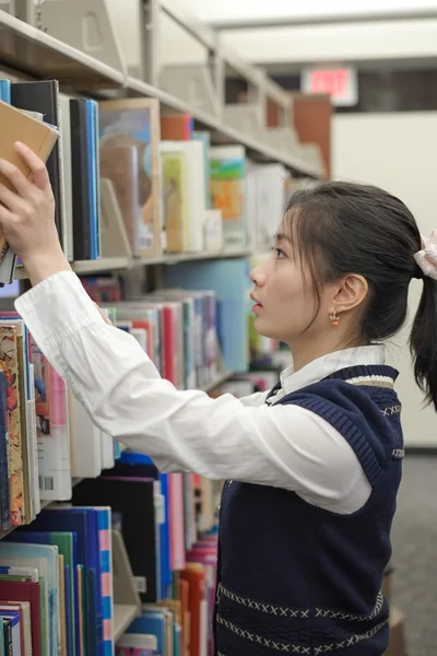 Mujer tomando un libro de estantería de la biblioteca —  Fotos de Stock