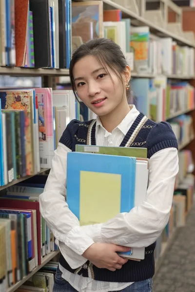 Joven estudiante sosteniendo libros cerca de estantería —  Fotos de Stock