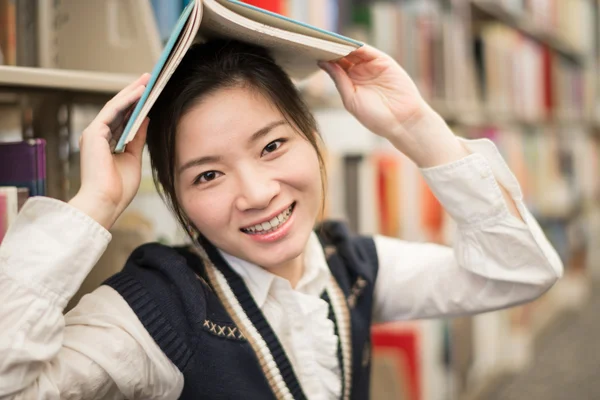 Meisje houden een boek over hoofd in de buurt van boekenplank — Stockfoto