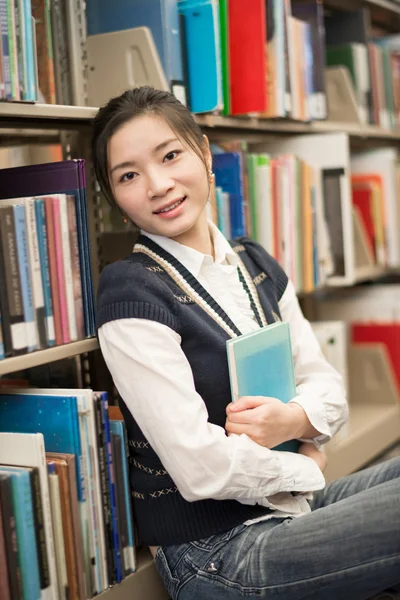 Mädchen umarmt ein Buch neben Bücherregal — Stockfoto