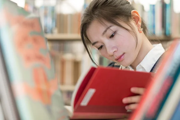 Estudiante leyendo un libro sobre estantería — Foto de Stock