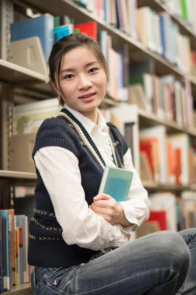 Mädchen umarmt ein Buch neben Bücherregal — Stockfoto