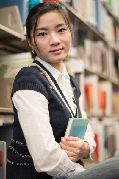 Mädchen umarmt ein Buch neben Bücherregal — Stockfoto