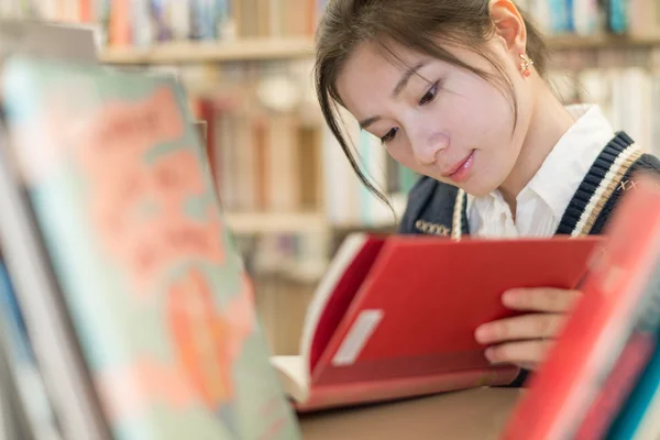 Student reading a book on bookshelf — Stock Photo, Image