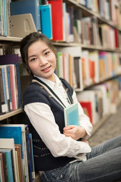 Mädchen umarmt ein Buch neben Bücherregal — Stockfoto