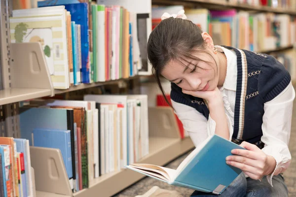 Vrouw lezen van een boek in de buurt van boekenplank — Stockfoto