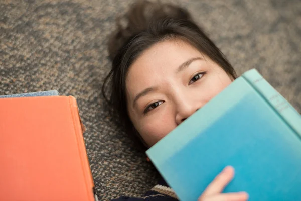 Student legt sich mit Büchern auf Teppich — Stockfoto