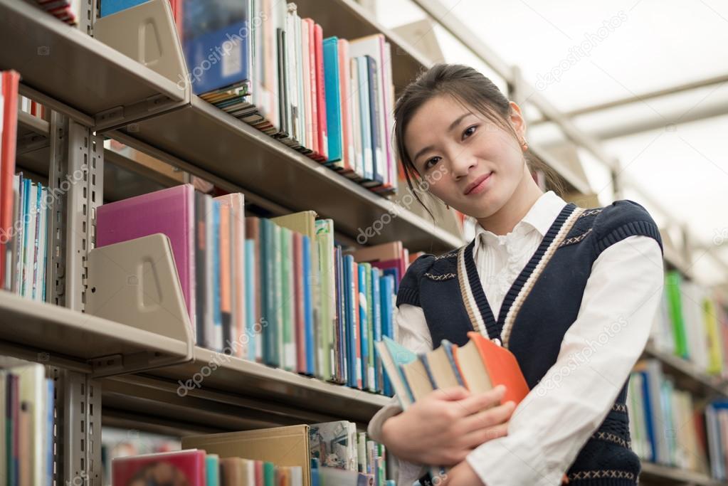 Student holding books next to bookshelf
