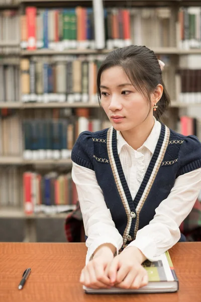 Gestresste Studentin sitzt in Bibliothek am Schreibtisch — Stockfoto