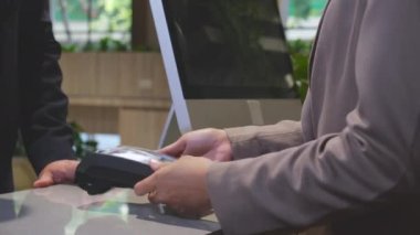 Kredi kartı alışverişini elinde tutan ve makine teknolojisi, alım-satım ve ödeme için temassız ödeme yapan işadamlarının elleri, kasiyer, nakitsiz toplum, iş konsepti.