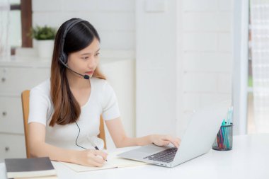 İnternette kulaklık takan genç Asyalı bir kadın. Masasında e-öğrenme, kulaklık takan bir kız. Evde dizüstü bilgisayarla interneti öğrenen bir kız..