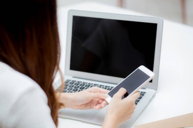 Evde dizüstü bilgisayar ve akıllı telefon modeliyle çalışan genç bir kadının eli. Not defteri ve telefon boş ekran, serbest arama. İnternet, iş ve iletişim konseptine bakın..