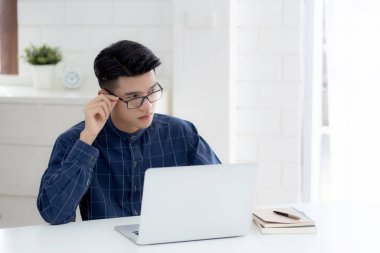 Gözlüklü genç bir iş adamı masada dizüstü bilgisayarla çalışıyor, serbest çalışan bir erkek masadaki iletişim için not defterini kullanıyor, girişimci işe başlıyor, yeni normal bir iş..