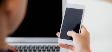 Evde dizüstü bilgisayar ve akıllı telefon modeliyle çalışan genç adamın eli. Not defteri ve telefon boş ekran, serbest arama. İnternet, iş ve iletişim konseptine bakın..