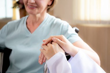Doktor kadın, yaşlı hastaların hastanede tekerlekli sandalyeye oturmasını, doktorların yaşlıları, teşhis hastalıklarını ve hastalıkları teskin etmek için el ele tutuşmalarını ve bakmalarını teşvik ediyor..