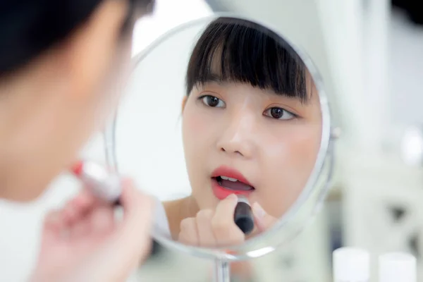 美丽的年轻亚洲女人在嘴唇上涂上红色口红 漂亮的女孩在镜子前看着镜子 用优雅的唇彩化妆 构成了女性的性感 护肤和健康的概念 — 图库照片