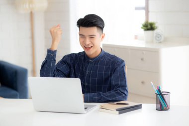 Mutlu genç iş adamı dizüstü bilgisayar işini evde heyecanlı ve başarılı bir şekilde bitiriyor, iş adamı başarıyla ve sürprizle dolu bir not defteri kullanıyor, serbest ya da çalışan, memnun ve memnun..
