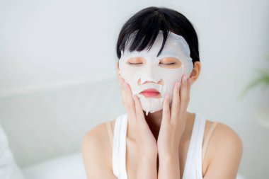 Yüzünde çarşaf maskesi olan güzel bir Asyalı kadın. Güzellik uzmanı. Yüzü kırışıklık, cilt bakımı, nemlendirici, sağlık ve sağlık için makyaj yapıyor..