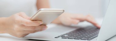 Laptop bilgisayarında çalışan ve evdeki masada internet üzerinden akıllı telefon okuyan genç bir kadın, sosyal medya, iş ve iletişim konsepti ile telefon kullanan serbest çalışan bir kız..