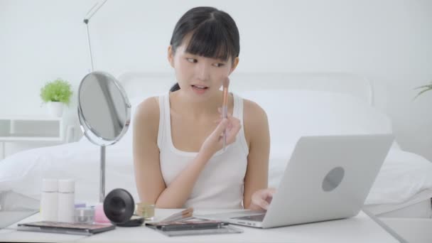在笔记本电脑上用笔刷着腮帮子学习化妆的年轻亚洲女人的美 在线辅导课程 女性在流媒体上的教学和解释化妆 — 图库视频影像