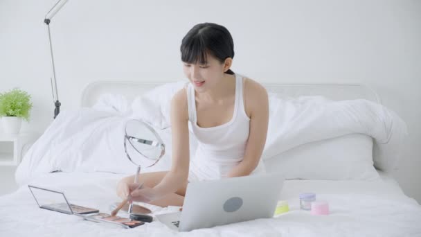 在笔记本电脑上用刷子在床上讲授课程 在流线型社交媒体上用化妆品化妆的年轻亚洲女人的美丽 — 图库视频影像