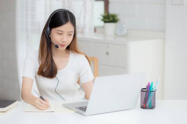 İnternette kulaklık takan genç Asyalı bir kadın. Masasında e-öğrenme, kulaklık takan bir kız. Evde dizüstü bilgisayarla interneti öğrenen bir kız..