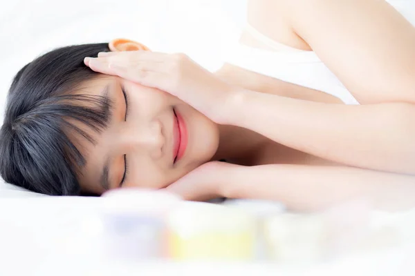 若いアジアの女性の美しい笑顔とベッドルームでベッドに横たわっ 衛生と健康と女の子のタッチ頬の美しさ クリームと化粧水 化粧品や化粧品 スキンケアとライフスタイルの概念 — ストック写真