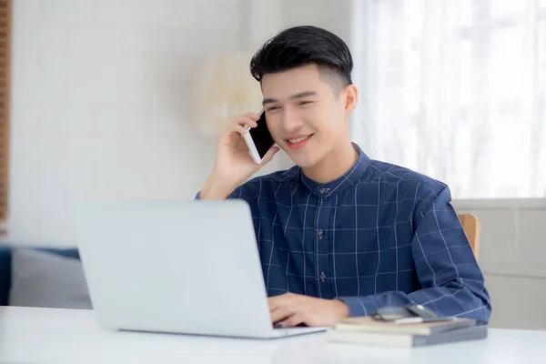 아시아인 남자가 전화를 노트북 컴퓨터를 가지고 집에서 일하고 노트북을 사용하여 — 스톡 사진
