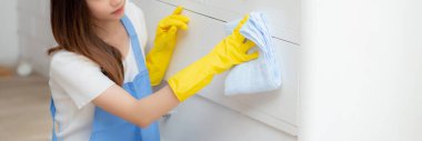 Yüz maskesi takan genç Asyalı kadın ve odada evi temizleyen eldivenler, hizmetçi ve hizmetçi, işçi tozu, ev işi ve ev işi, yaşam tarzı konsepti, afiş web sitesi.