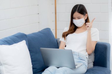 Yüz maskeli Asyalı genç bir iş kadını bilgisayardan internete, oradan oturma odasına, oradan tıbbi maskeli bir kız ve kovid-19 için karantinaya alma fikrini ve çalışmasını düşün..