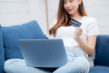 Genç Asyalı kadın internette dizüstü bilgisayarla internetten internet alışverişi yapıyor. Mutlu kız ödemesi kanepe, alışveriş ve ödeme, iş konsepti..