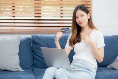 Genç Asyalı kadın internette dizüstü bilgisayarla internetten internet alışverişi yapıyor. Mutlu kız ödemesi kanepe, alışveriş ve ödeme, iş konsepti..