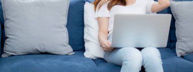 Genç Asyalı güzel bir kadın dizüstü bilgisayarda çalışıyor ve evdeki kanepede fikir üretiyor. Serbest çalışan bir kız kanepede oturuyor. Oturma odasında internetten internet kullanıyor..