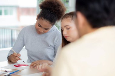 Bir grup öğrenci okulda öğretmenle birlikte oturuyor, çalışıyor ve resim çiziyor, öğrencilerin yaratıcılığı ve gelişimi kursta, okula, eğitim konseptine geri dönüyor..