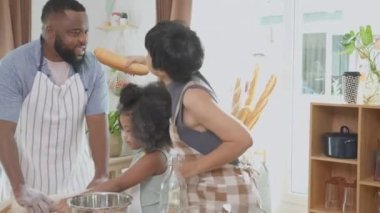 Afro-Amerikan ailesi yemek pişirmek, dans etmek ve şarkı söylemek için önlük takıyor. Anne ve baba ve küçük çocuk, eğlenceli ve neşeli bir şekilde yemek ve şarkı hazırlıyorlar..