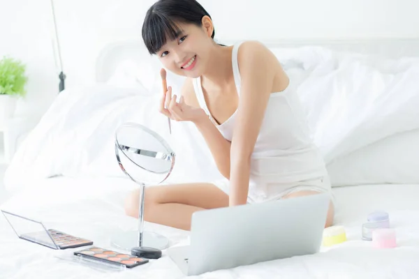 若いアジアの女性の美しさは ベッドの上でオンラインチュートリアルコースとラップトップコンピュータ上の頬にブラシでメイクを学び 女性の教育とストリーミングソーシャルメディア上の化粧品で構成を説明します — ストック写真