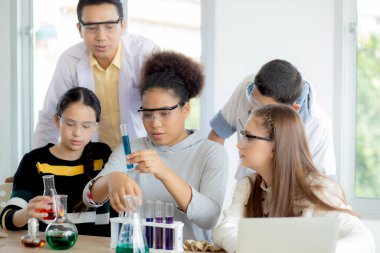 Genç öğretmen grup öğrencilerine okulda sıvı için bilim ve test kimyasalları öğretiyor, çocuklar laboratuarda deney bilimi okuyor ve öğreniyor, eğitim konsepti.
