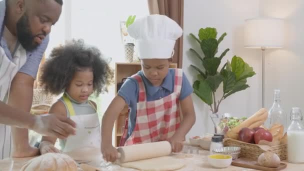 非洲裔美国人家庭 儿子和女儿一起在家里的厨房里翻来覆去 为父亲做饭准备脱粒面粉 父母和小孩也一起准备有趣的食物 — 图库视频影像