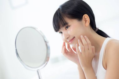 Mutlu gülümseyen ve yanak aynasına dokunan güzel Asyalı bir kadının güzel yüzü. Cilt bakımı, cilt bakımı, cilt bakımı ve sağlıklı bir konsepti olan güzel bir yüz makyajı..